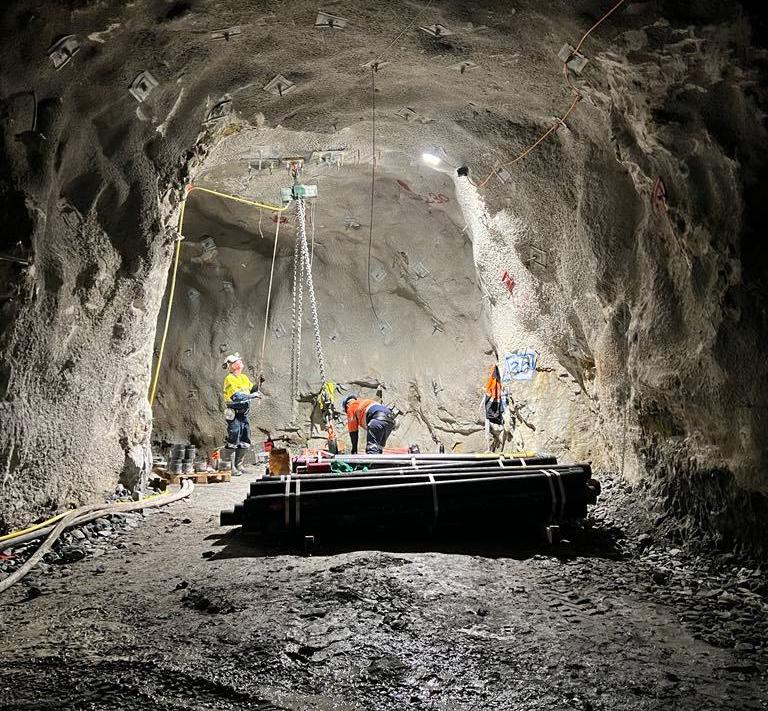 Crews handling casing pipes underground in a rock tunnel