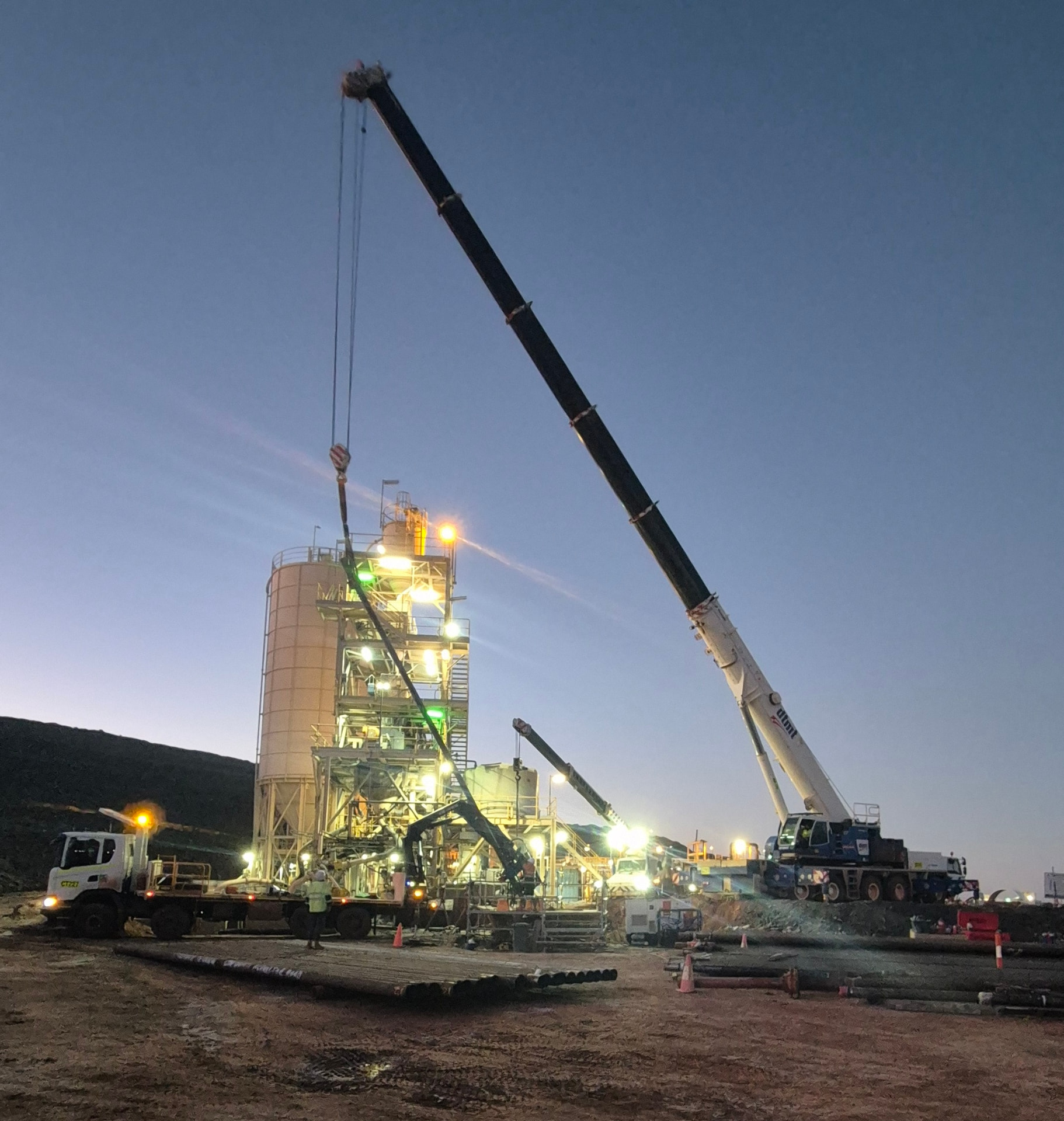 Large crane lifting casing at a floodlit mine site at dusk