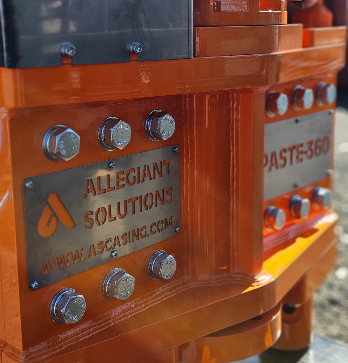Close-up of Allegiant Solutions and PASTE-360 nameplates bolted to an orange wellhead assembly