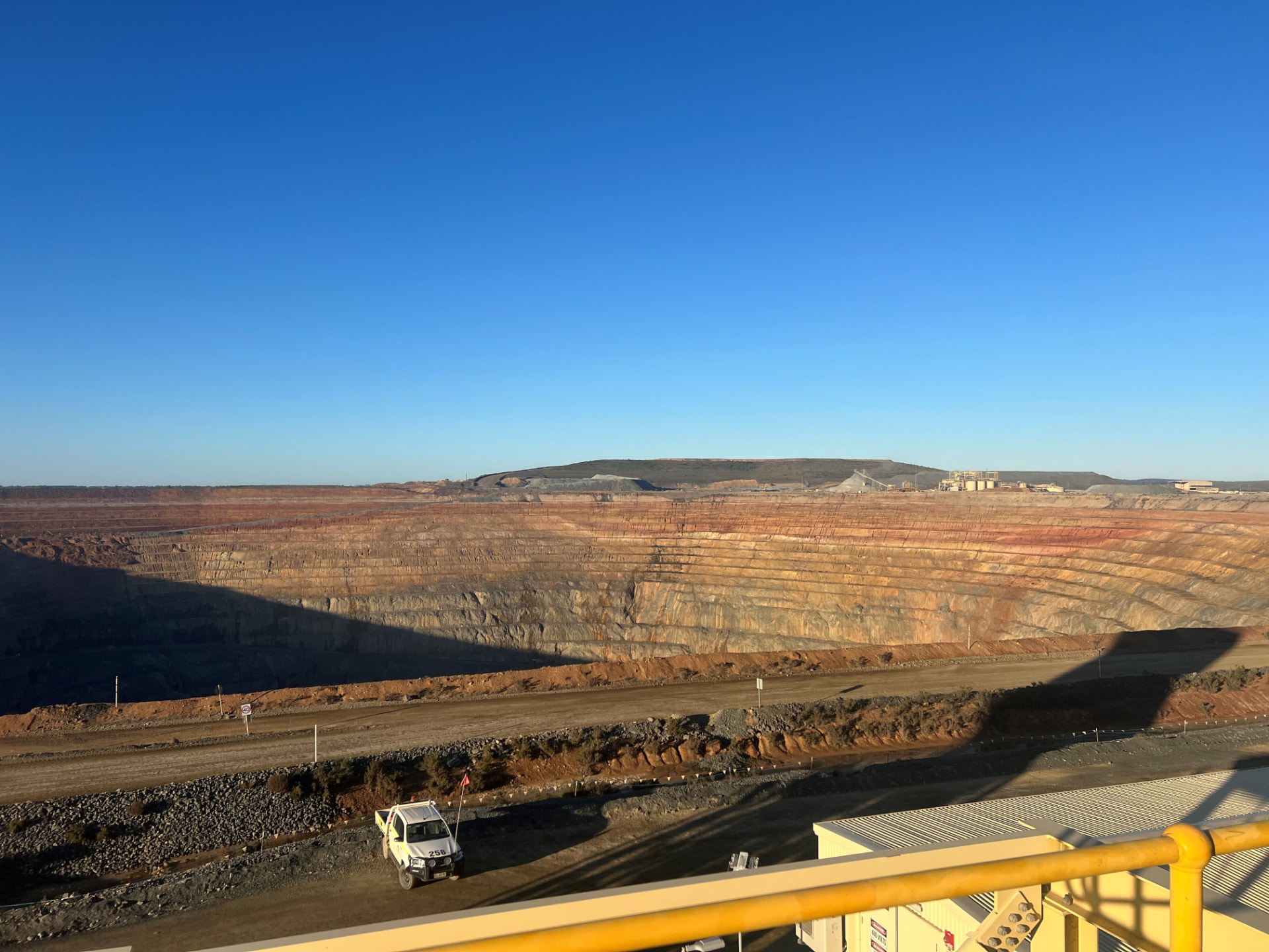 Open-pit mine with terraced walls and an Allegiant site vehicle on the haul road