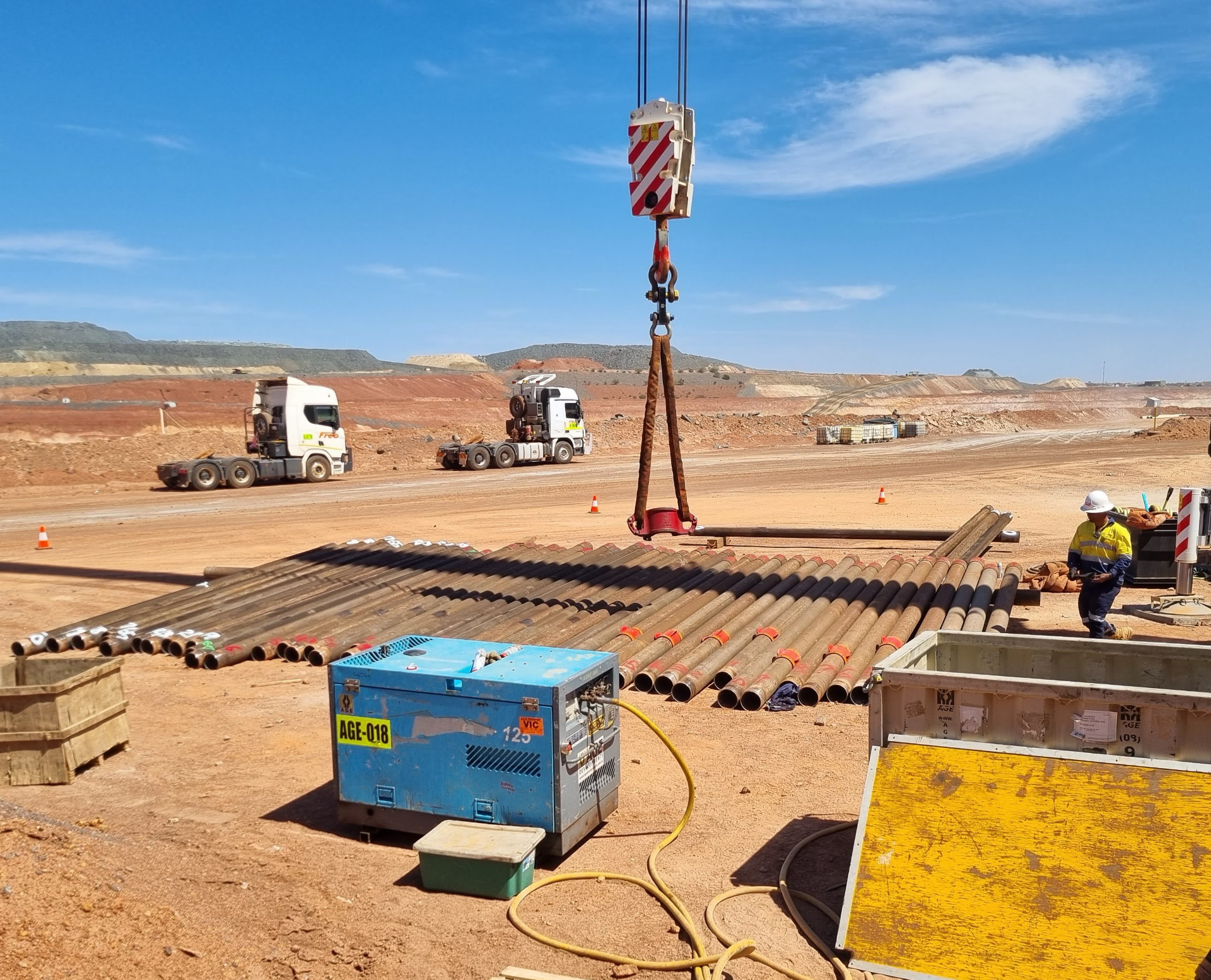 Casing pipes laid out on a mine site while a crane lifts a casing shoe